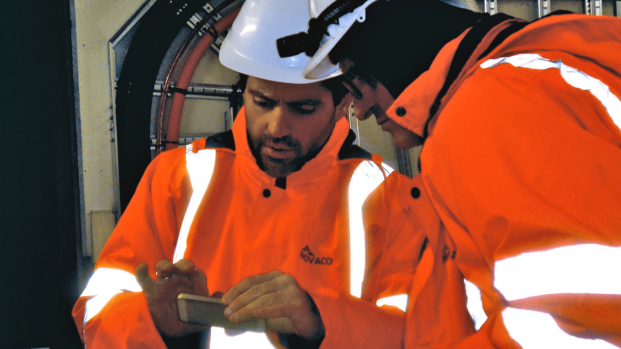 NOVACO EMPLOYEES IN UNIFORMS CONCENTRATING ON LOOKING AT A MOBILE SCREEN